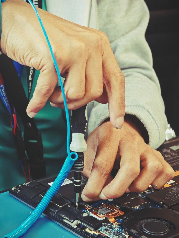 Close-up of a technicians hands repairing a laptops internal components with tools.